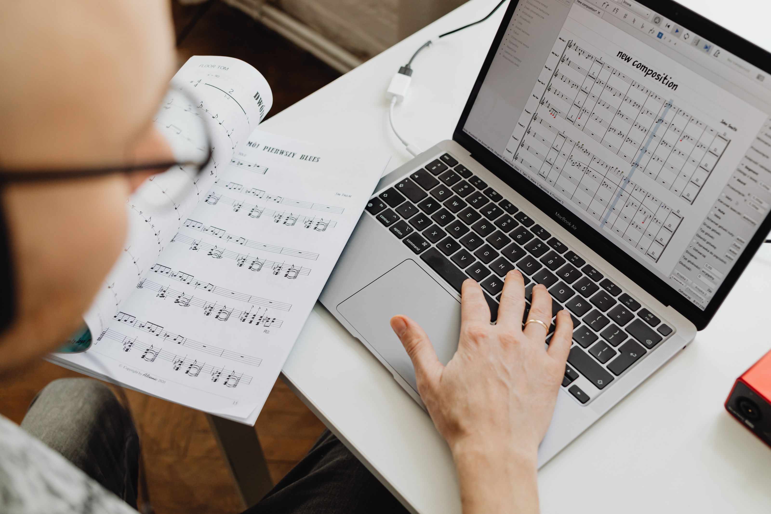 Eine Person arbeitet mit Notenheft und Notationssoftware an einer Komposition.