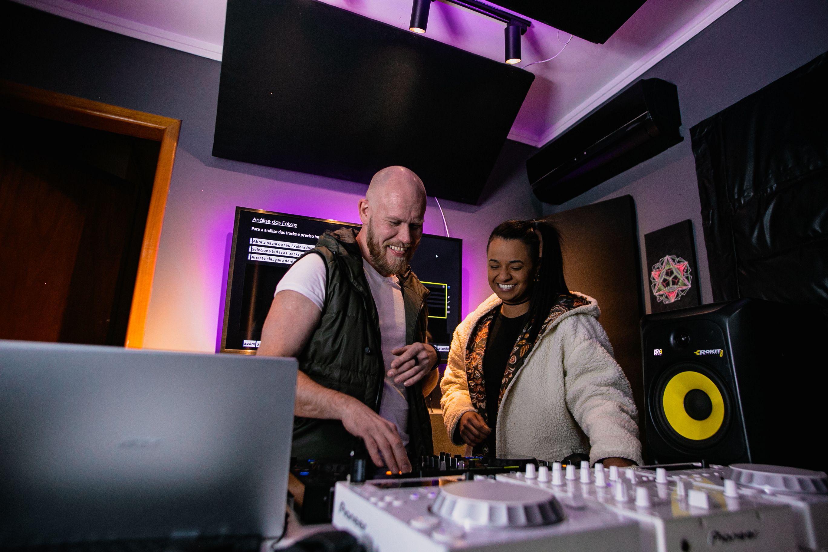 Zwei Musiker:innen arbeiten lachend gemeinsam in einem Tonstudio.
